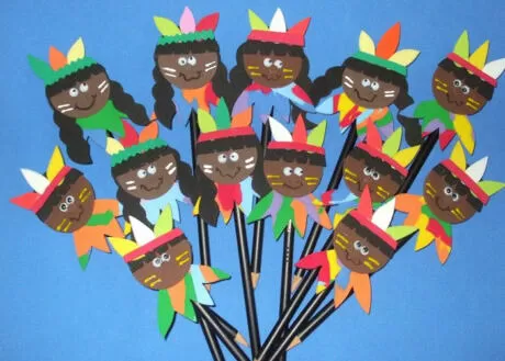 Bonecos de papel coloridos representando indígenas, com penas e rostos sorridentes.